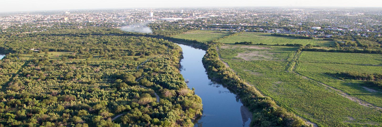 Rio Grande River cutting through forested land and farmland with city on the horizon