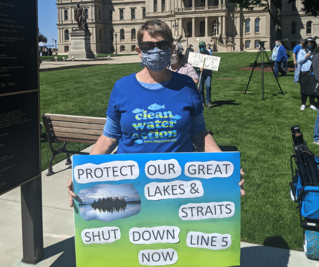 Woman outside Michigan Capitol wearing clean water action shirt and sign: "Protect our Great Lakes & Straits - Shut Down Line 5 Now"