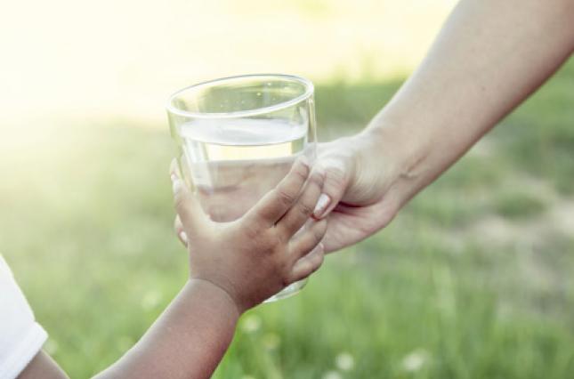 Handing a glass of water to a child. Photo credit: iStock