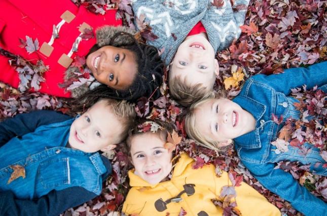 Kids in rain jackets lying in a bed of leaves - canva image