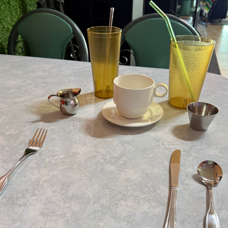 Table setting with metal utensils, porcelain coffee cup, and reusable cups