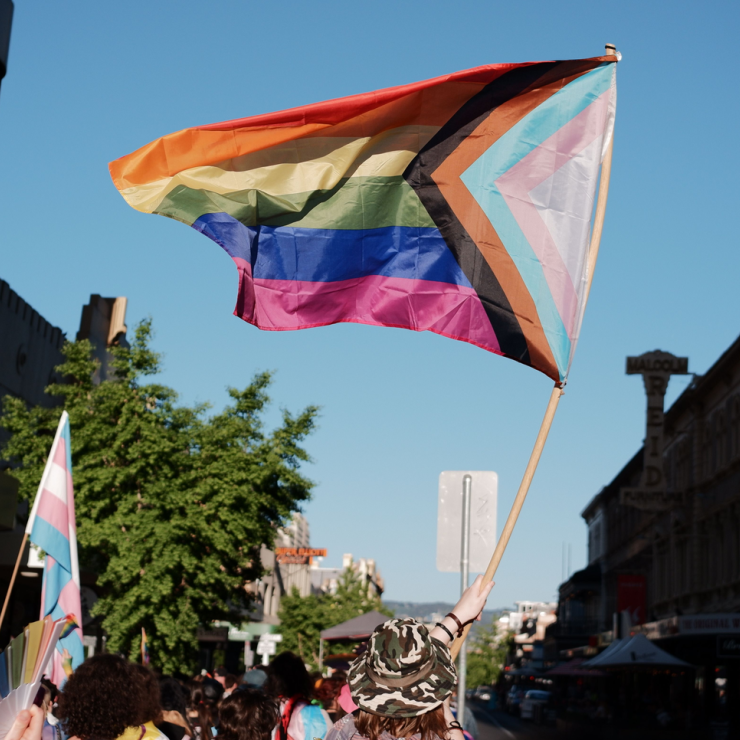 A progress pride flag being held up in a public event among other pride flags