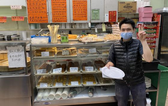 ReThink Disposable business partner poses with new reusable dishware in front of display case of Chinese pastry