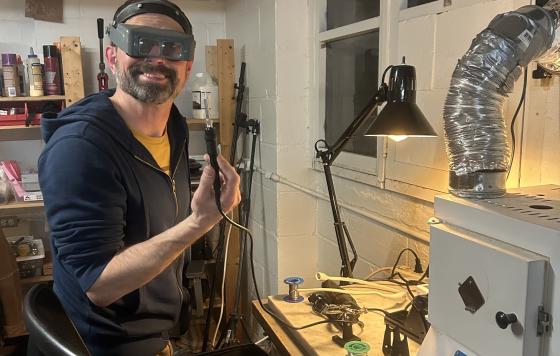 A volunteer wearing safety glasses posing in front of a electronics repair project